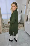 Mulher usando um casaco cardigan ambicione by anselmi alongado verde matcha , com fendas, combinado com uma blusa branca e calças brancas.