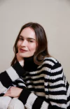 Modelo usando blusa feminina listrada em preto e off white, com detalhes em tricô e gola alta.