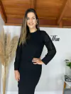 Mulher sorrindo usando um cropped tricô vazado preto, posando em um ambiente decorado com plantas e elementos de moda.