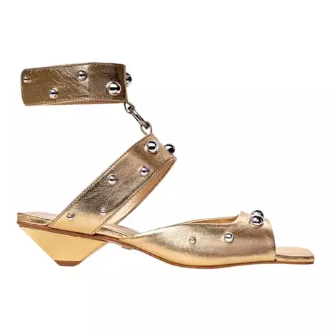 Sandália feminina dourada com salto baixo, tiras em couro metalizado e aplicação de tachas - modelo moderno com tornozeleira, ideal para looks fashion e ousados - Carrano 