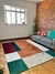 Tapete geométrico Porto com cores terracota, verde, vinho, bege gold, azul marinho e off-white em uma sala de estar moderna com sofá cinza e parede de tijolos aparentes.