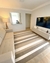 Tapete listrado em veludo nas cores off-white, taupe e bege gold em sala de estar moderna com sofá e televisão.