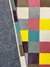 Tapete geométrico com quadrados coloridos em tons de granito, cacau, amarelo, natural, Tiffany, uva, rosa e verde claro, com fundo antiderrapante.