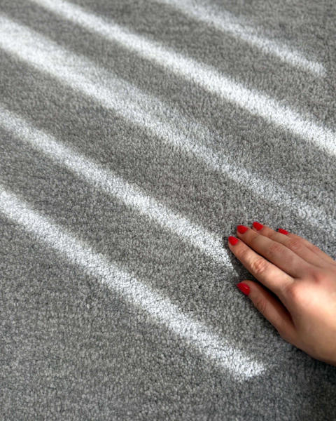 Tapete retangular para sala na cor prata e cinza da Coleção Bruma, com textura macia em nylon Econyl e luz natural incidindo sobre a superfície.