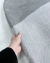 Tapete de nylon com bordas orgânicas em tons de cinza e prata sendo segurado por uma mão.