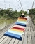 Tapete em várias cores disposto em uma ponte de madeira, com uma pessoa ao fundo segurando-o.