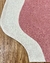 Tapete em nylon com bordas orgânicas, nas cores off-white e rosé, sobre piso de madeira.