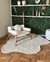 Tapete liso off-white em nylon com bordas orgânicas em uma sala decorada com cadeira e prateleiras.