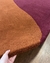 Tapete em nylon nas cores bordô e terracota sendo levantado por uma mão.
