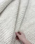 Tapete de fibra natural off-white com trama grossa, confeccionado em tear manual, sendo segurado por uma mão, Tapetes São José