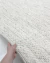 Tapete de fibra natural em tons off-white e bege, feito à mão, sendo segurado por uma mão, Tapetes São José