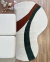 Tapete em nylon com bordas orgânicas nas cores off-white, terracota e verde escuro, colocado em piso de madeira ao lado de móveis.