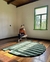Tapete Urbano de Nylon com bordas orgânicas em verde e verde escuro Econyl, em uma sala com janela e piso de madeira.