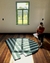 Tapete com listras verdes e verde escuro em nylon, bordas orgânicas, colocado em sala iluminada.