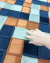 Mão tocando tapete redondo da Coleção Trançado, com quadrados em azul, verde e terracota, tapetes sao josé