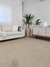 Tapete Quadrados de Veludo Francês Marrom Claro em sala de estar moderna, com sofá bege e plantas decorativas.