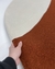 Tapete com bordas orgânicas em nylon nas cores off-white e terracota, sendo segurado por uma mão.