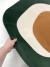 Tapete orgânico da coleção Ellos em verde, off-white e terracota sendo segurado por uma mão, mostrando detalhes do material de veludo.
