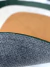 Detalhe do tapete orgânico da coleção Ellos, mostrando a parte inferior antiderrapante em veludo, nas cores verde, off-white e terracota.