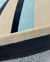 Tapete retangular em tecido com as cores em bege, preto, tiffany e off-white, ao lado de um sofá bege, Tapetes São José