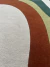 Detalhe do tapete orgânico com design em curvas nas cores bege, terracota, verde musgo e verde escuro