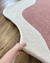 Tapete de nylon com bordas orgânicas nas cores off-white e rosé sendo levantado para mostrar textura.