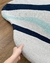 Tapete com bordas orgânicas em tons de prata, azul marinho e Tiffany, feito de nylon Econyl, sendo segurado por uma mão sobre um piso de madeira.