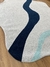 Tapete com bordas orgânicas em tons de prata, azul marinho e Tifanny, feito de nylon Econyl, sobre piso de madeira.