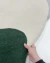 Mão segurando tapete Stone com bordas orgânicas nas cores off-white e verde escuro, São José.