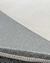 Detalhe do tapete cinza e prata, destacando a textura e a borda costurada.