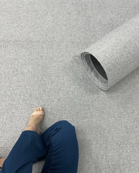 Tapete em Linho Mesclado Cinza desenrolado no chão, com detalhe de uma pessoa de calça azul sentada ao lado, São José.