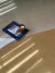 Tapete retangular com blocos de cores mostarda, musgo e bege, com uma vela e uma revista CASA sobre ele