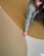 Tapete retangular para sala com design em blocos de cores mostarda, musgo e bege, com mulher sentada sobre ele tocando o tapete