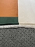 Detalhe do Tapete Harmonia com bordas arredondadas nas cores verde, terracota e off-white, mostrando textura e acabamento.