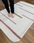 Tapete em nylon com listras nas cores off-white, mostarda, rosé e lilás, colocado em um piso de madeira.