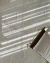 Tapete retangular off-white da Coleção Ecos, feito de nylon Econyl, com textura suave e detalhes em relevo, decorando sala de estar com cadeira ao lado.