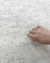 Detalhe de uma mão tocando o tapete orgânico na cor palha da Coleção Placas, mostrando a textura macia do veludo e o acabamento sofisticado do produto para sala, Tapetes São José