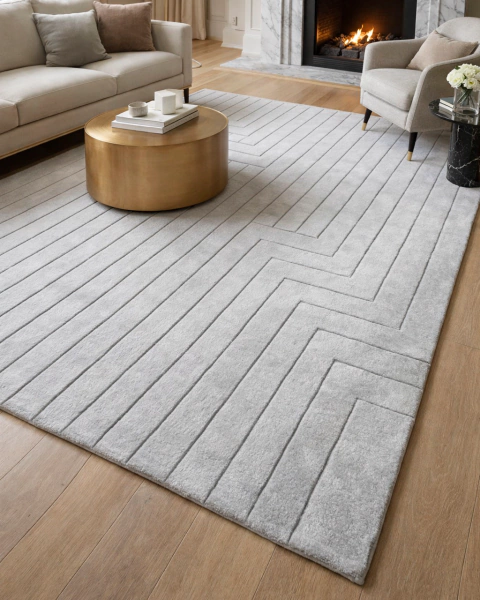 Tapete retangular para sala nas cores prata e cinza, com listras em relevo, posicionado em ambiente moderno com sofá claro e mesa de centro dourada.