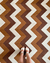 Tapete Chevron Bouclé Atenas nas cores bege, terra e chocolate com padrão geométrico e pés femininos em sandálias brancas sobre ele.