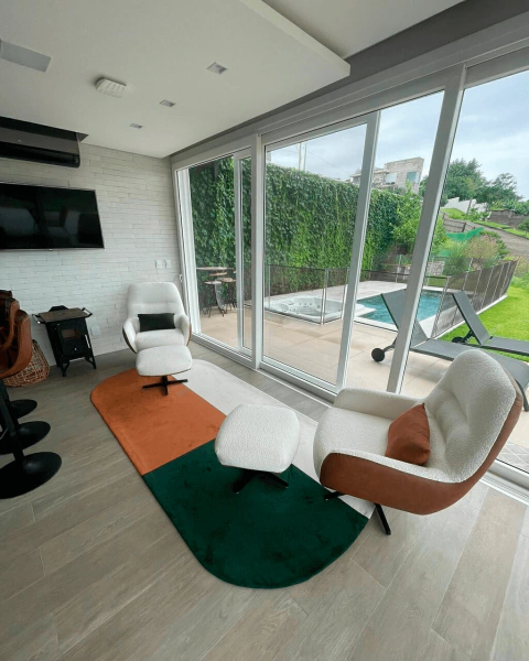Tapete com bordas arredondadas nas cores verde, terracota e off-white decorando uma sala moderna com poltronas e vista para área externa.
