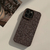 Funda Brownie para iPhone en color marrón, mostrando textura y diseño moderno, colocada sobre una superficie clara junto a un vaso de café.