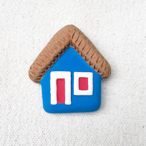 Casinha de parede decorativa feita de cerâmica, com telhado marrom e paredes azuis, apresentando janelas e porta brancas e vermelhas.