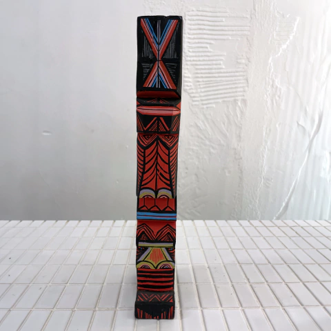 Escultura vertical colorida de madeira, com padrões geométricos e figuras estilizadas, criada por Célio Souza.