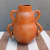Vaso de cerâmica Maragogipinho com duas alças, em tom terracota, exibido sobre uma superfície com listras.