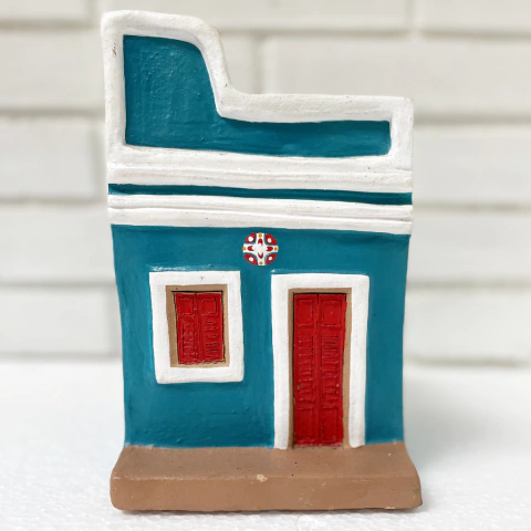 Escultura de uma casa em cerâmica nas cores azul e branco, com portas vermelhas e detalhes decorativos.