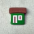 Casinha de parede decorativa em cerâmica com telhado marrom e paredes verdes e brancas.
