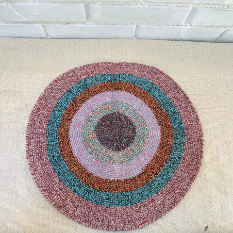 Lugar de mesa redondo com padrões coloridos em tons de azul, rosa e marrom, ideal para decoração e utilitário.