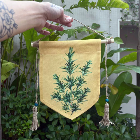 Banner amarelo com pintura de planta verde, segurado por uma mão, em um ambiente natural.