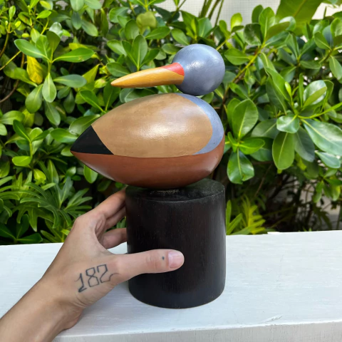 Escultura de um pássaro Martin Pescador da Mata em madeira, com cores variadas, apoiada em uma base preta.