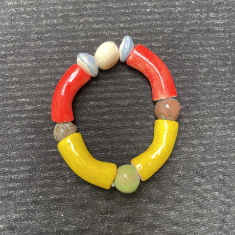 Pulseira de cerâmica colorida com detalhes em vermelho, amarelo e azul, sobre fundo escuro.